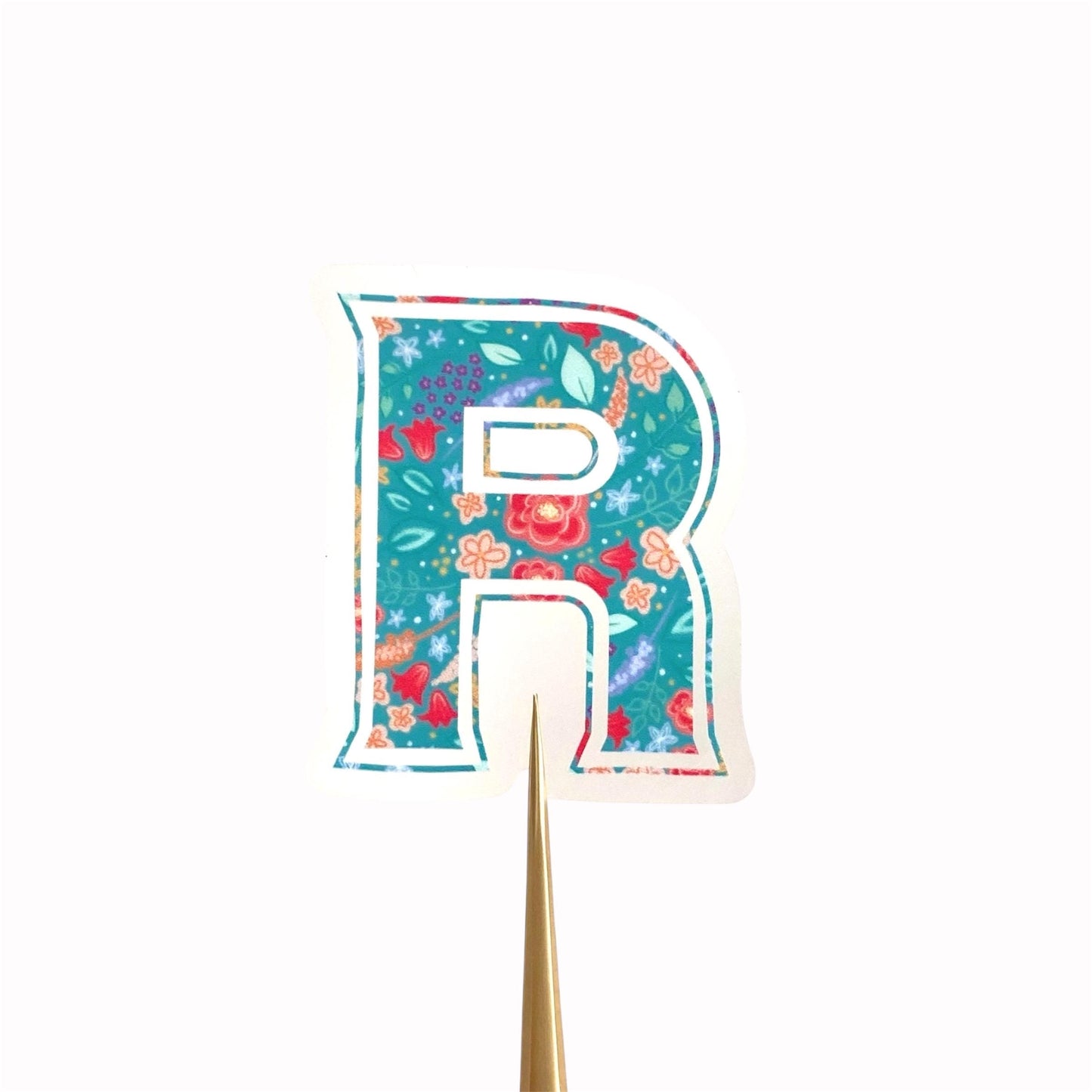 Clear sticker with a teal floral letter 'R' against a cream background.