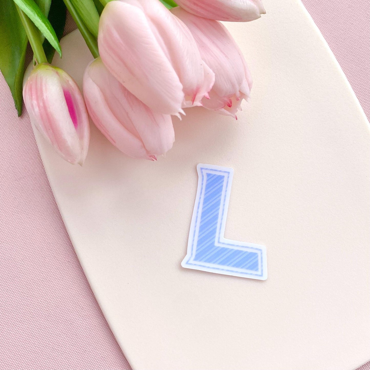 Pink tulips on a white board with a blue letter 'L' sticker on a pink background