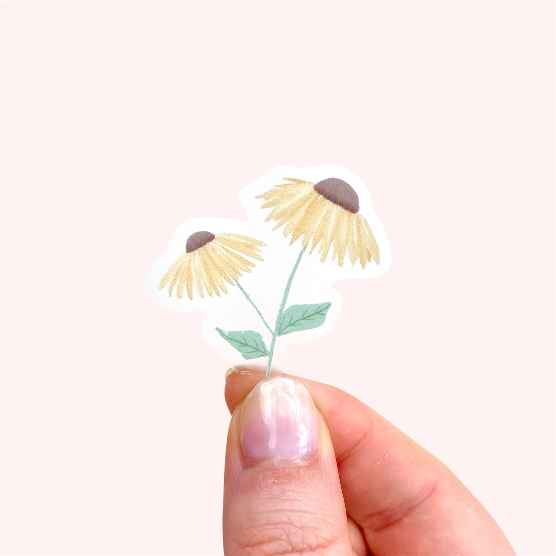 A sticker with 2 yellow daisies held by a hand against a pink background.