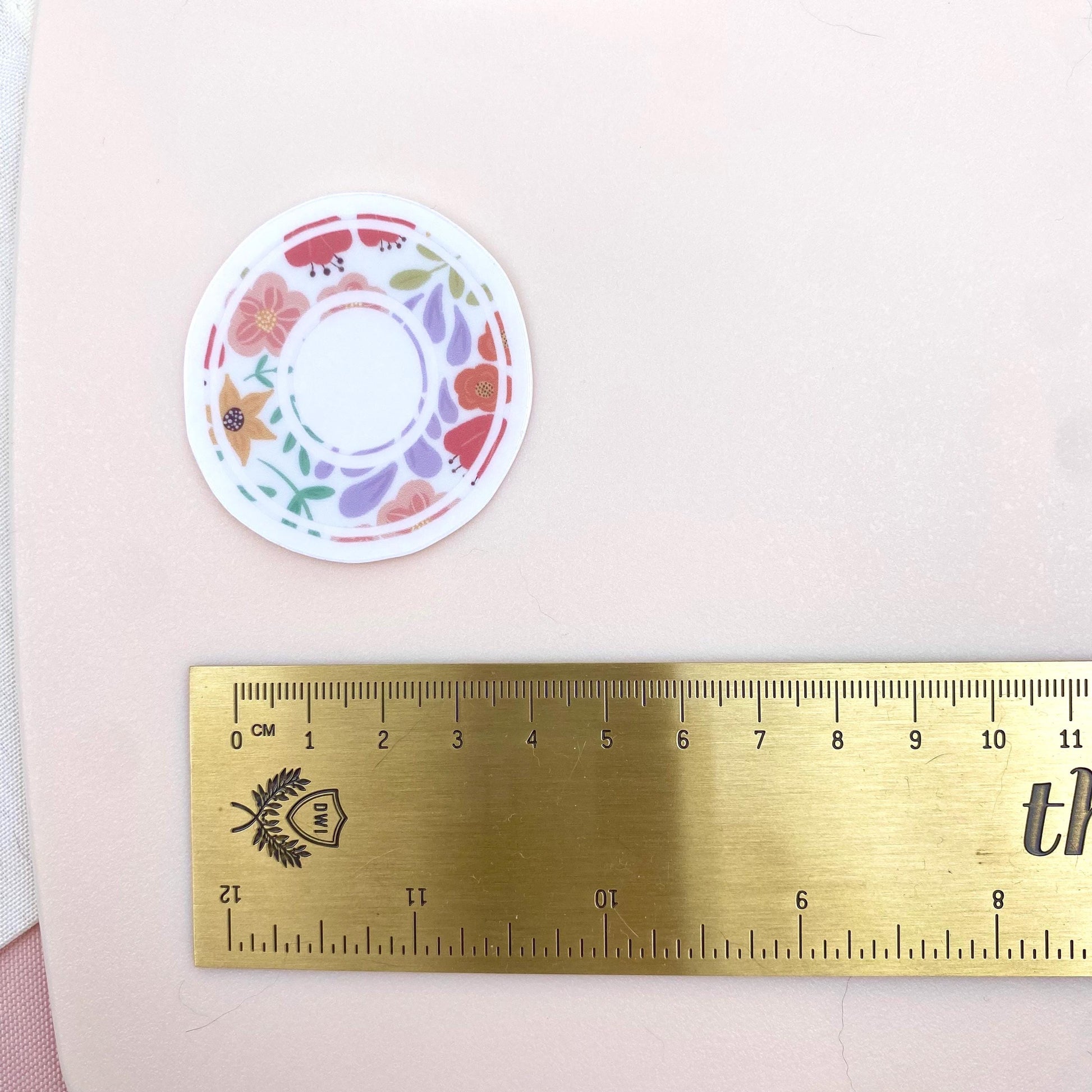 Decorative letter 'X' sticker with floral patterns on a light background with a gold ruler for scale.