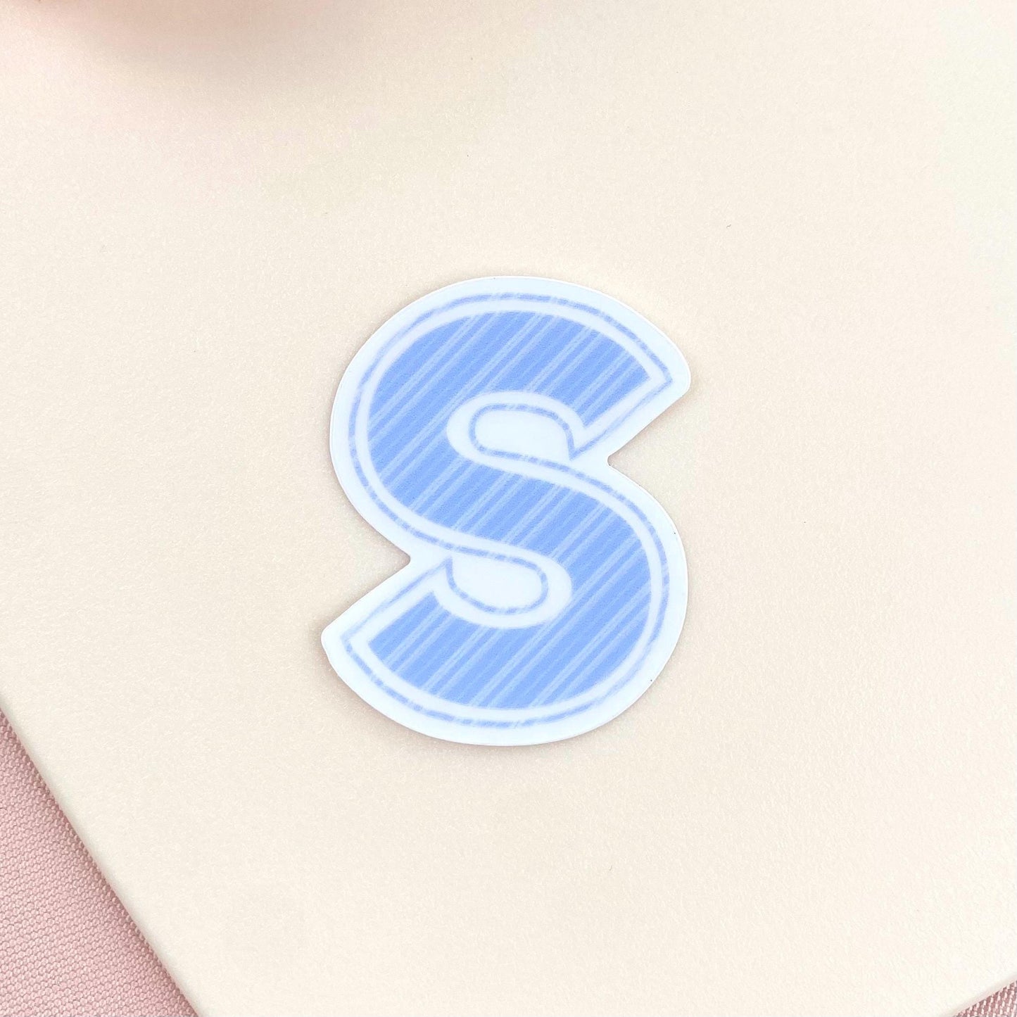 Blue striped letter 'S' sticker on a beige background