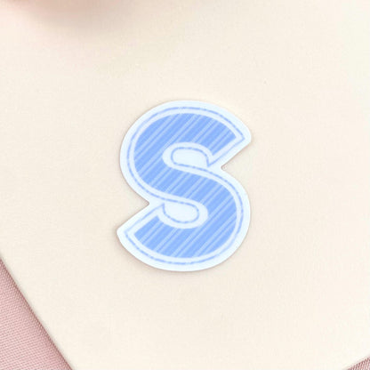 Blue striped letter 'S' sticker on a beige background