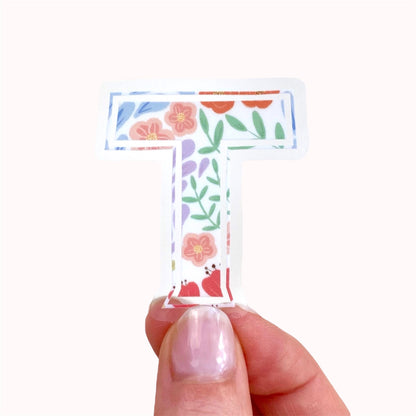 Floral letter 'T' sticker held by a hand on a white background