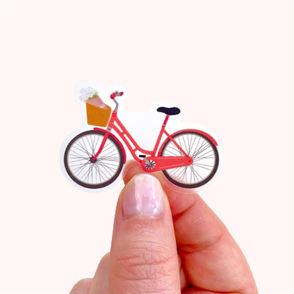 Pink bicycle sticker held by a hand against a cream background.