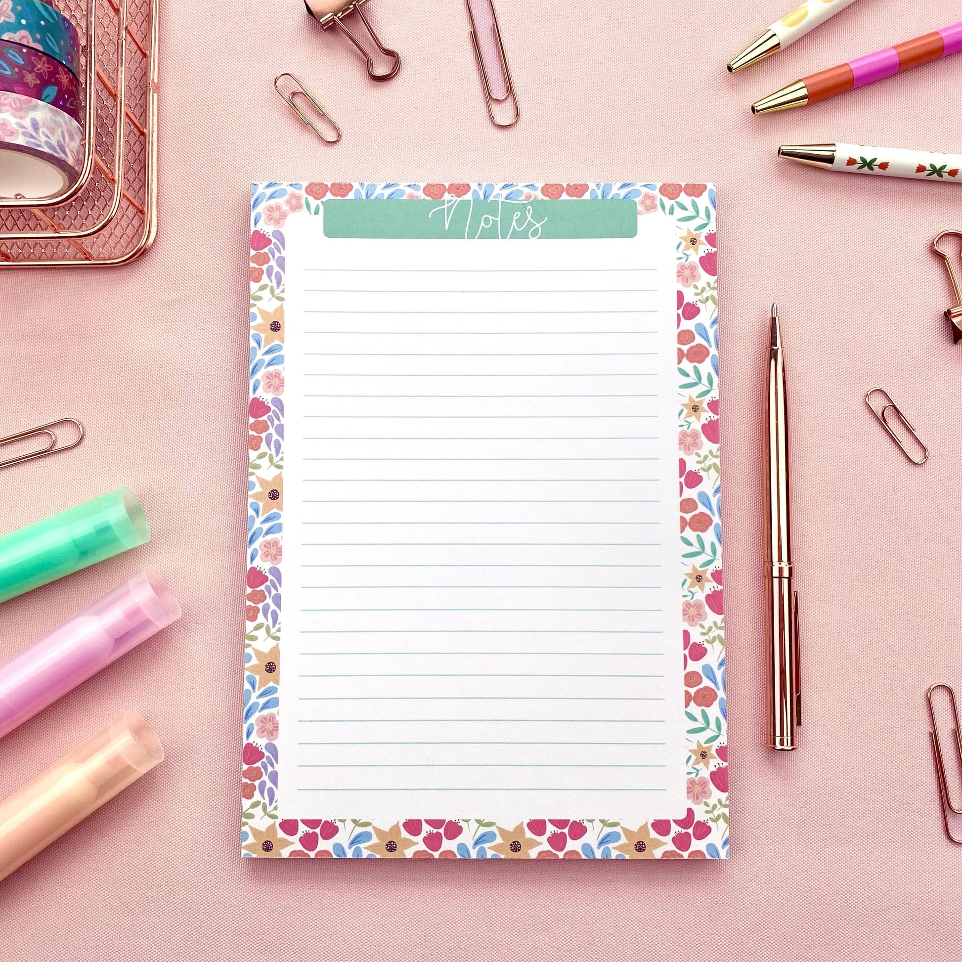 Floral border notepad with stationery items on a pink background