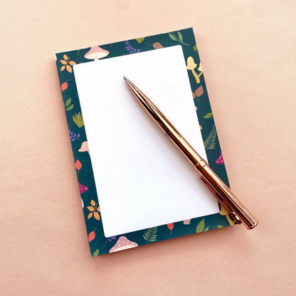 Notepad with mushroom and leaf patterned border on a white background with a rose gold pen