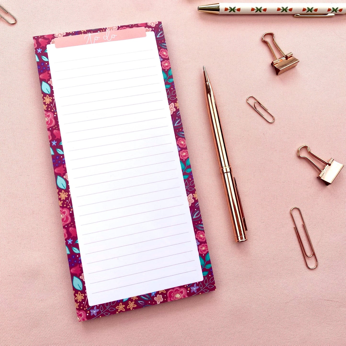 Floral-patterned notepad with a pen and paper clips on a pink background