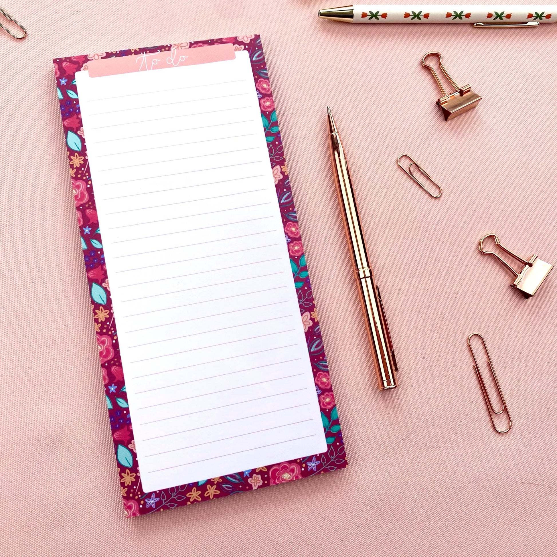 Floral-patterned notepad with a pen and paper clips on a pink background