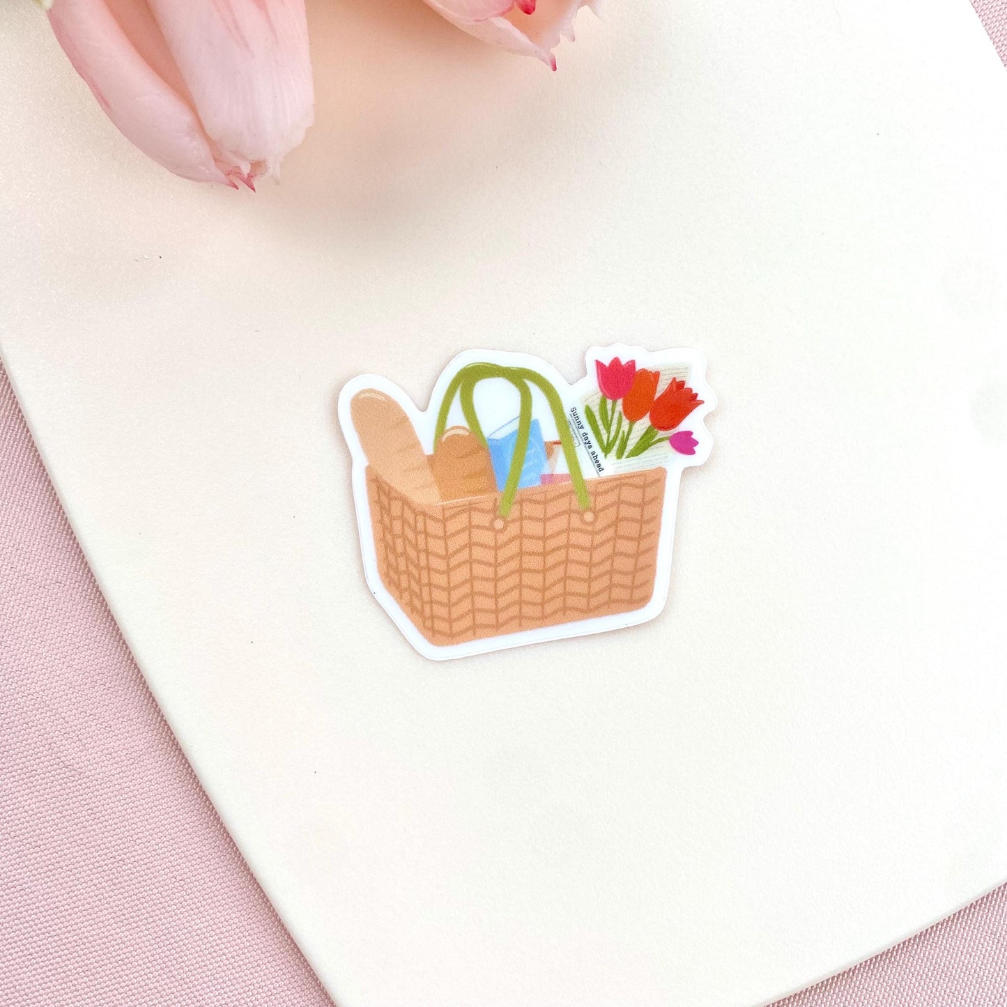 Sticker of a picnic basket with flowers and bread on a white surface.