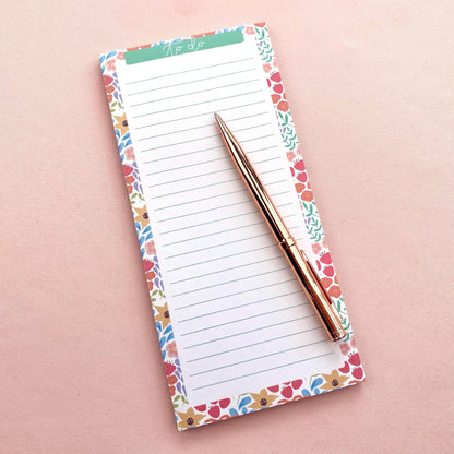 Floral-patterned notepad with a pen on a pink background