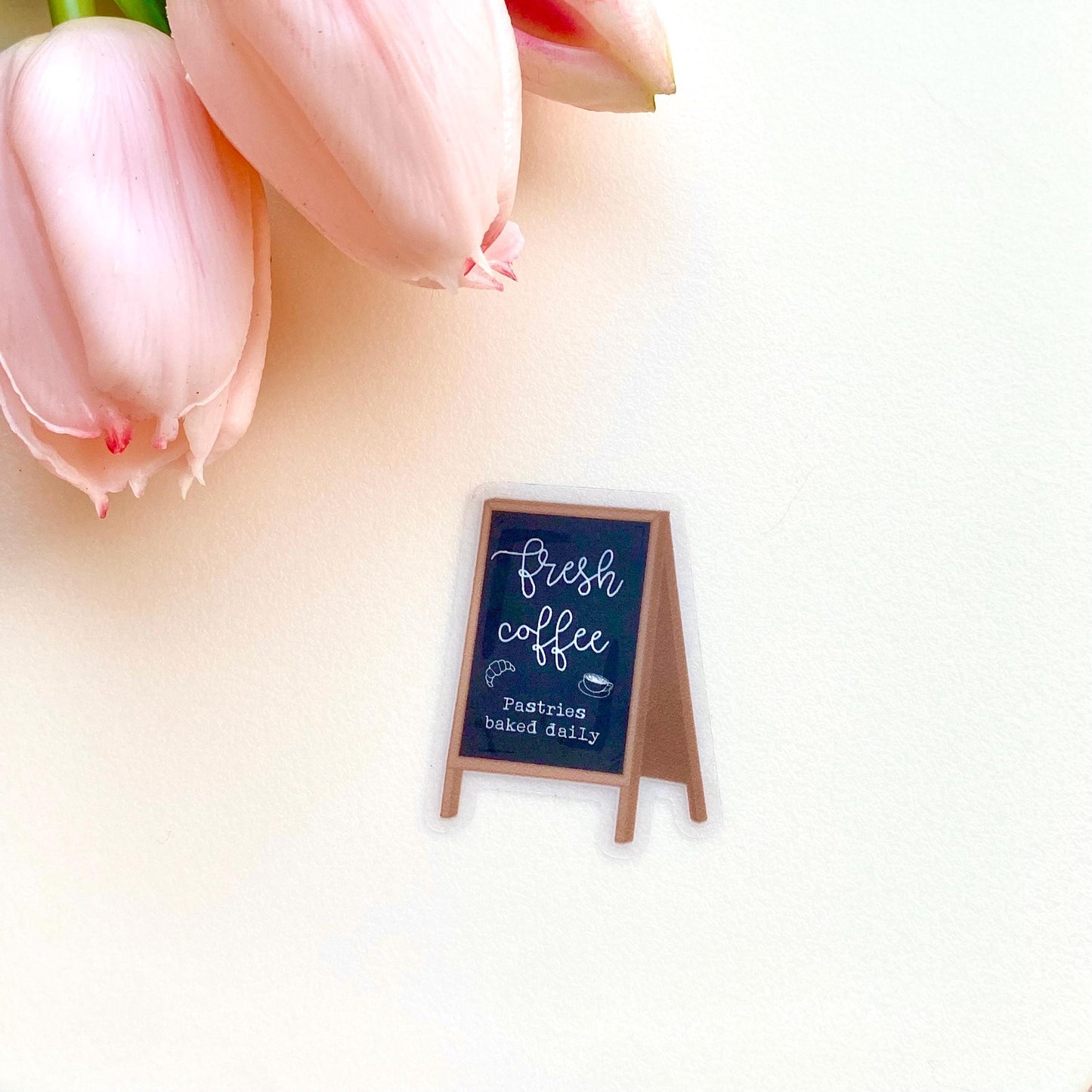 Sticker with a chalkboard sign held by a hand with 'Fresh coffee' and 'Pastries baked daily' text on a white background.