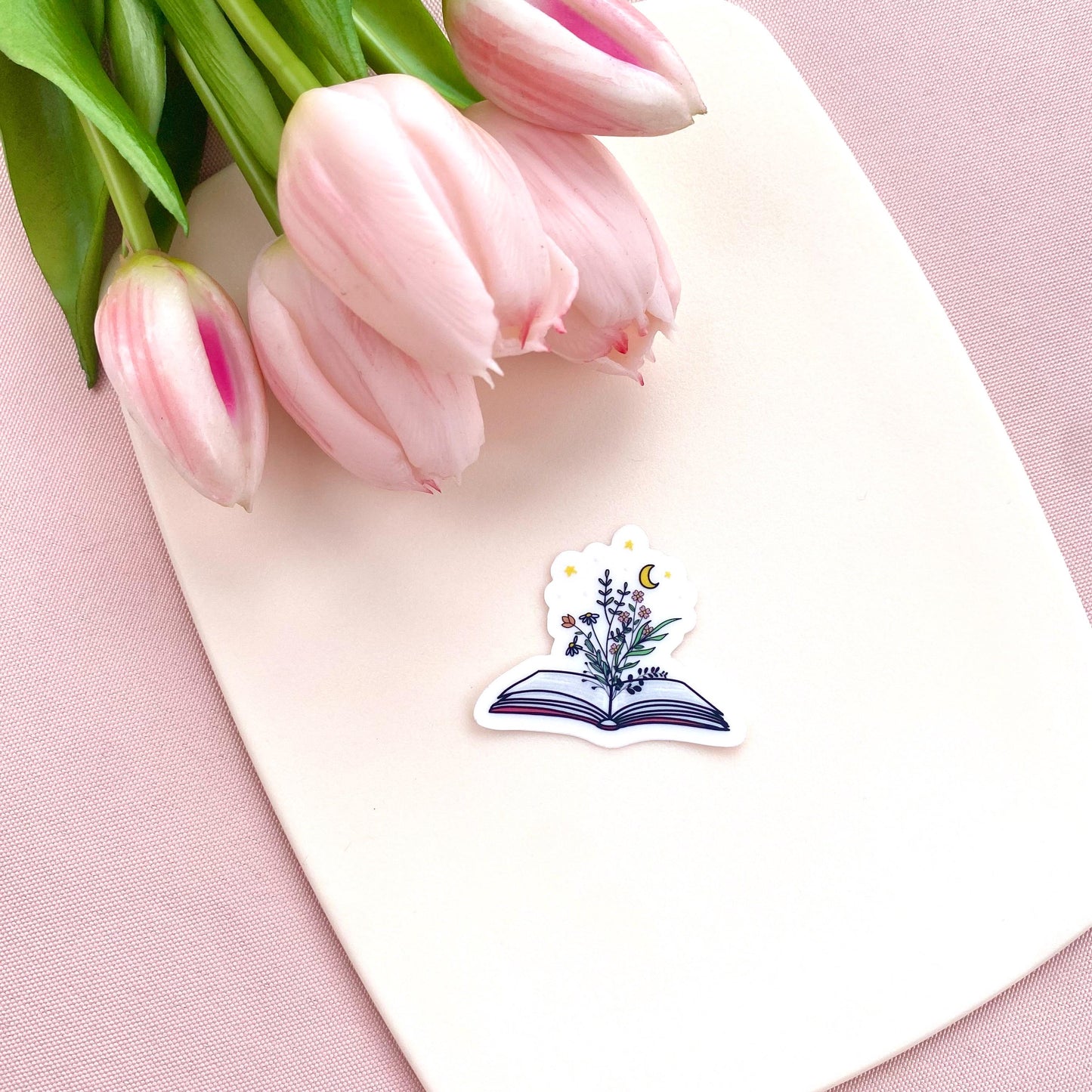Decorative sticker of an open book with floral designs and a moon and stars on a white background with pink tulips