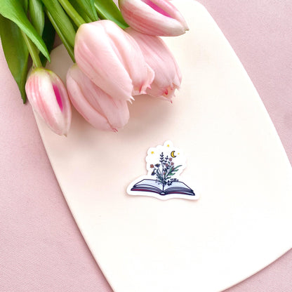 Decorative sticker of an open book with floral designs and a moon and stars on a white background with pink tulips