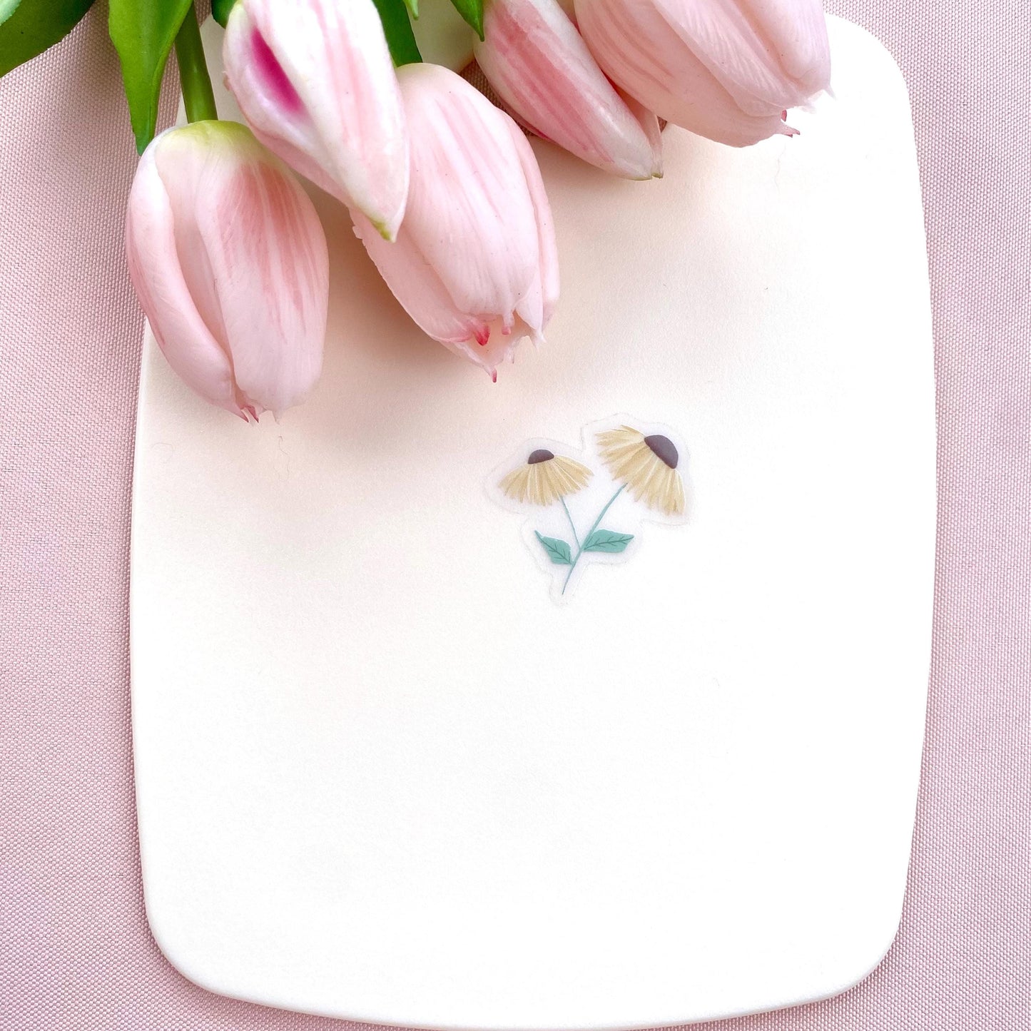 A sticker with 2 yellow daisies against a cream background with pink tulips.