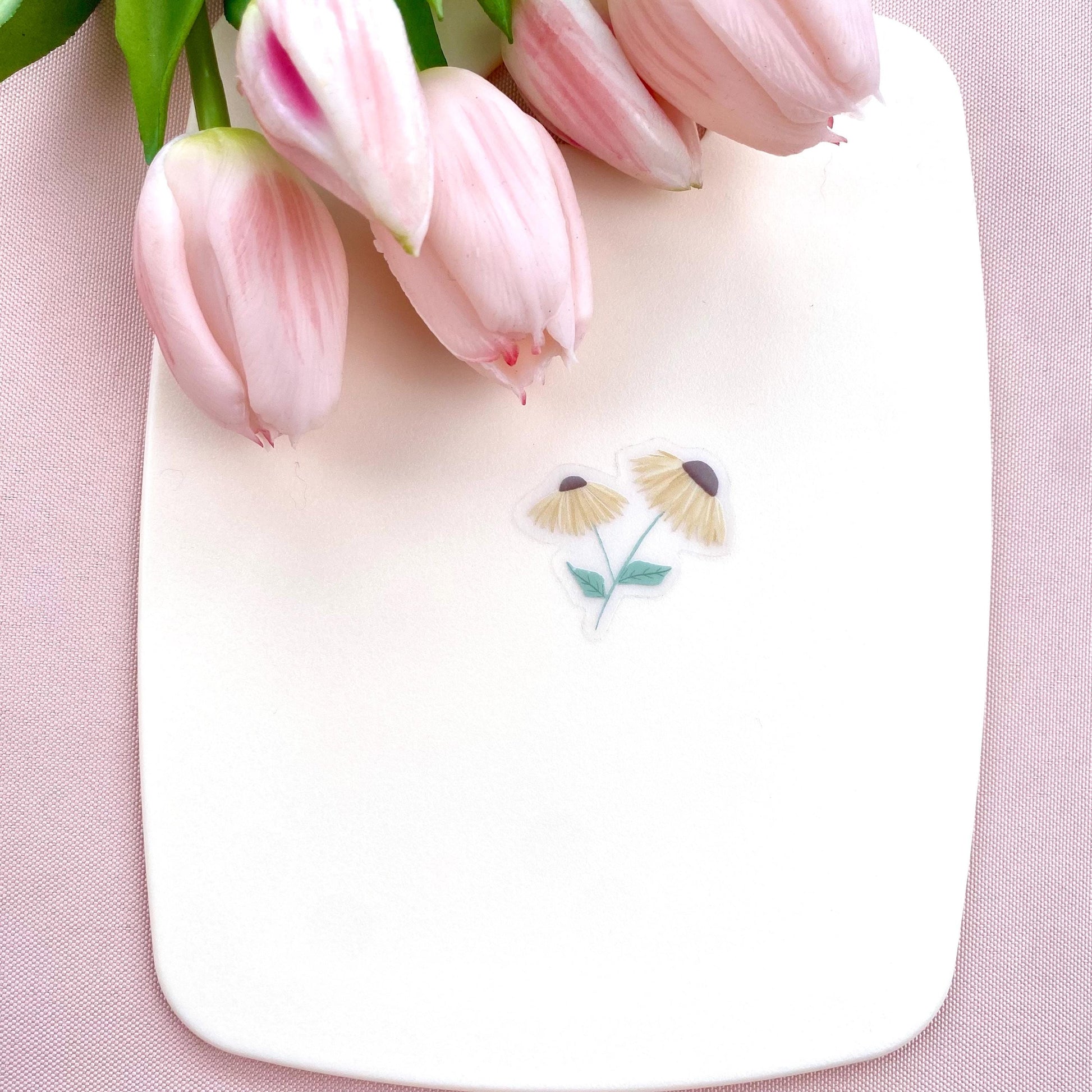 A sticker with 2 yellow daisies against a cream background with pink tulips.
