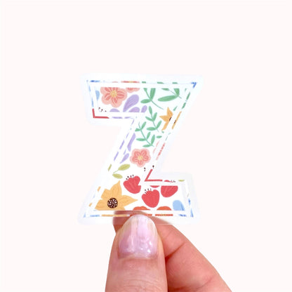 Decorative letter 'Z' sticker with floral patterns held by hand against a white background