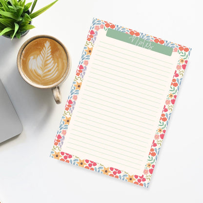 Floral notepad with a cup of coffee and laptop on a white surface