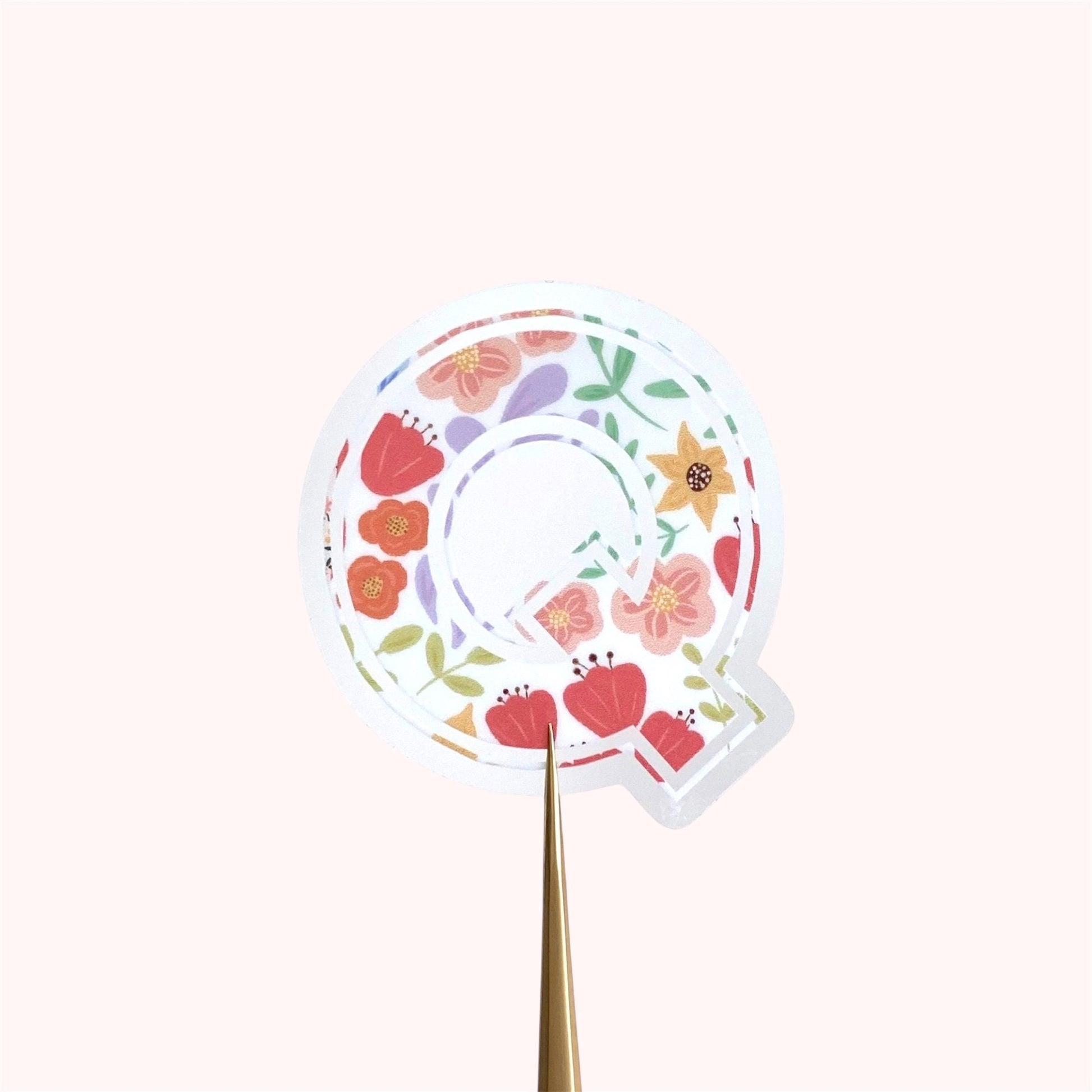 Decorative letter 'Q' sticker with floral patterns on a light background.