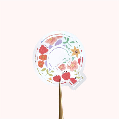 Decorative letter 'Q' sticker with floral patterns on a light background.