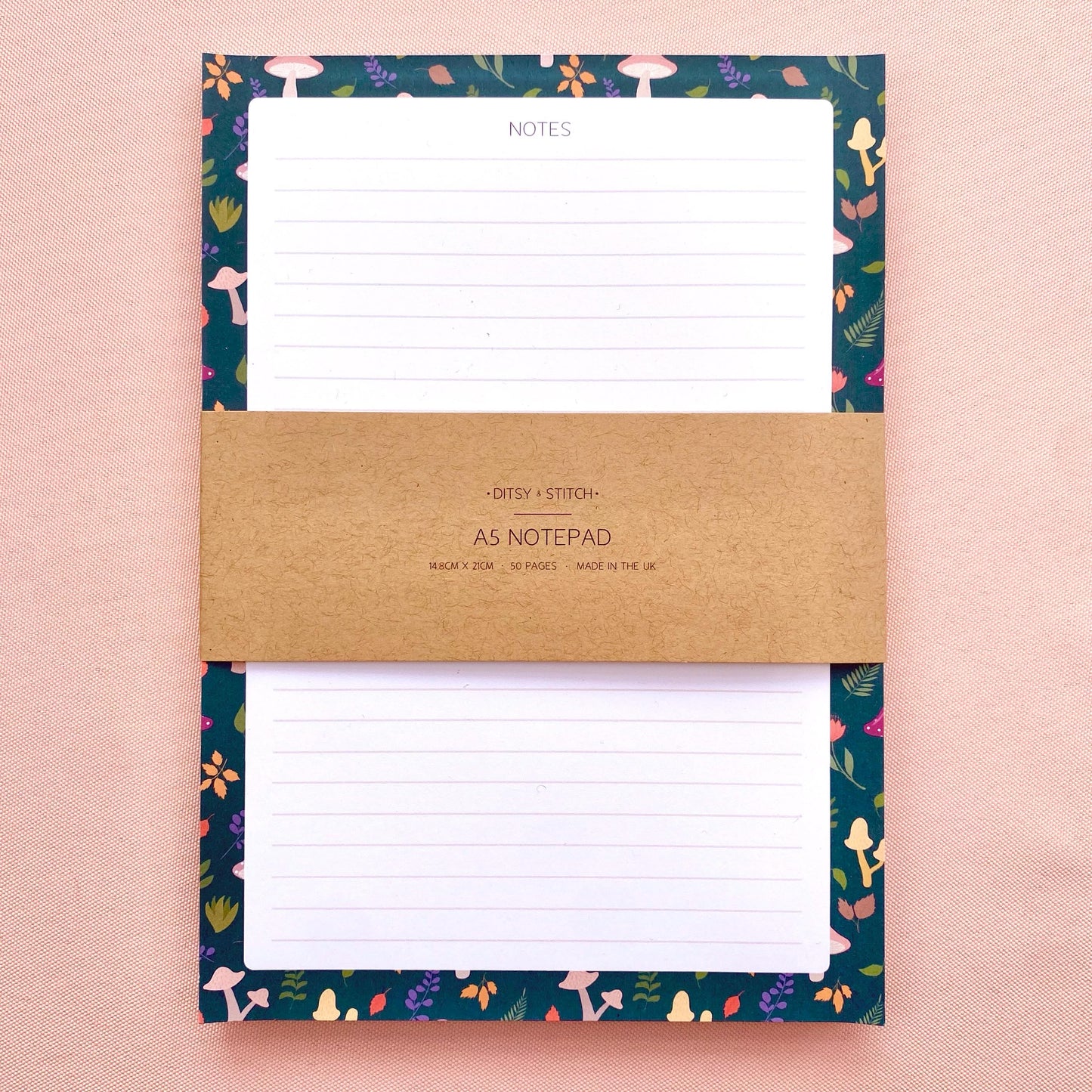 Lined notepad with a decorative blue border featuring mushrooms and leaves on a pink background