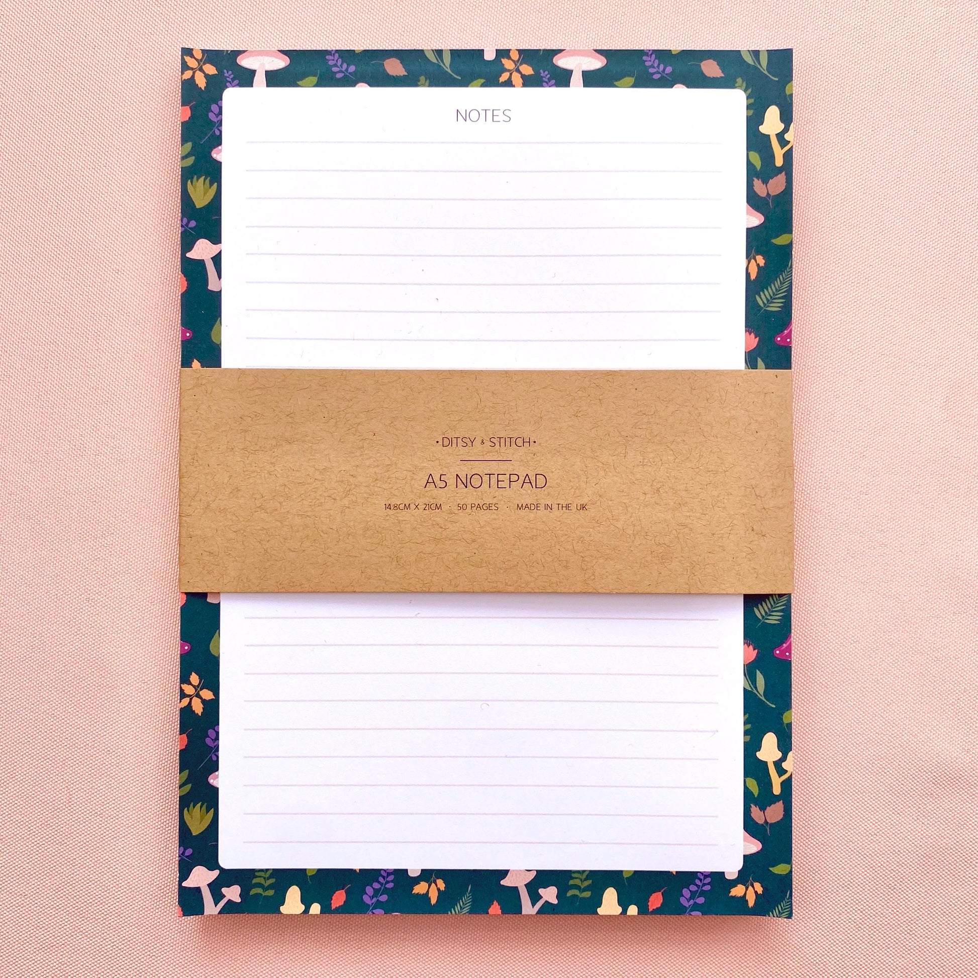 Lined notepad with a decorative blue border featuring mushrooms and leaves on a pink background