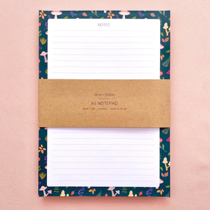 Lined notepad with a decorative blue border featuring mushrooms and leaves on a pink background