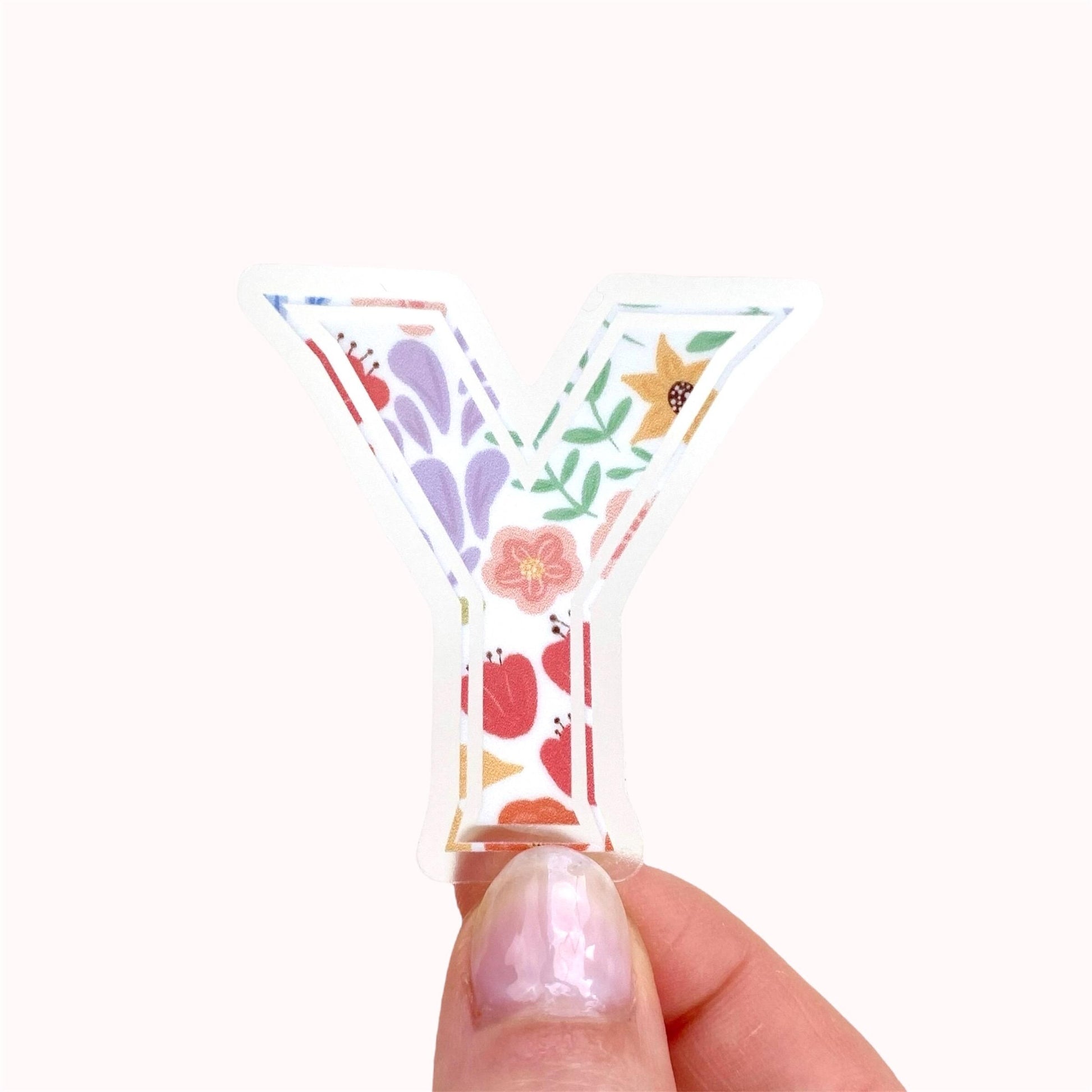 Decorative clear letter 'Y' sticker with floral patterns held by a hand on a white background