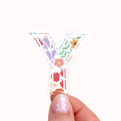 Decorative clear letter 'Y' sticker with floral patterns held by a hand on a white background