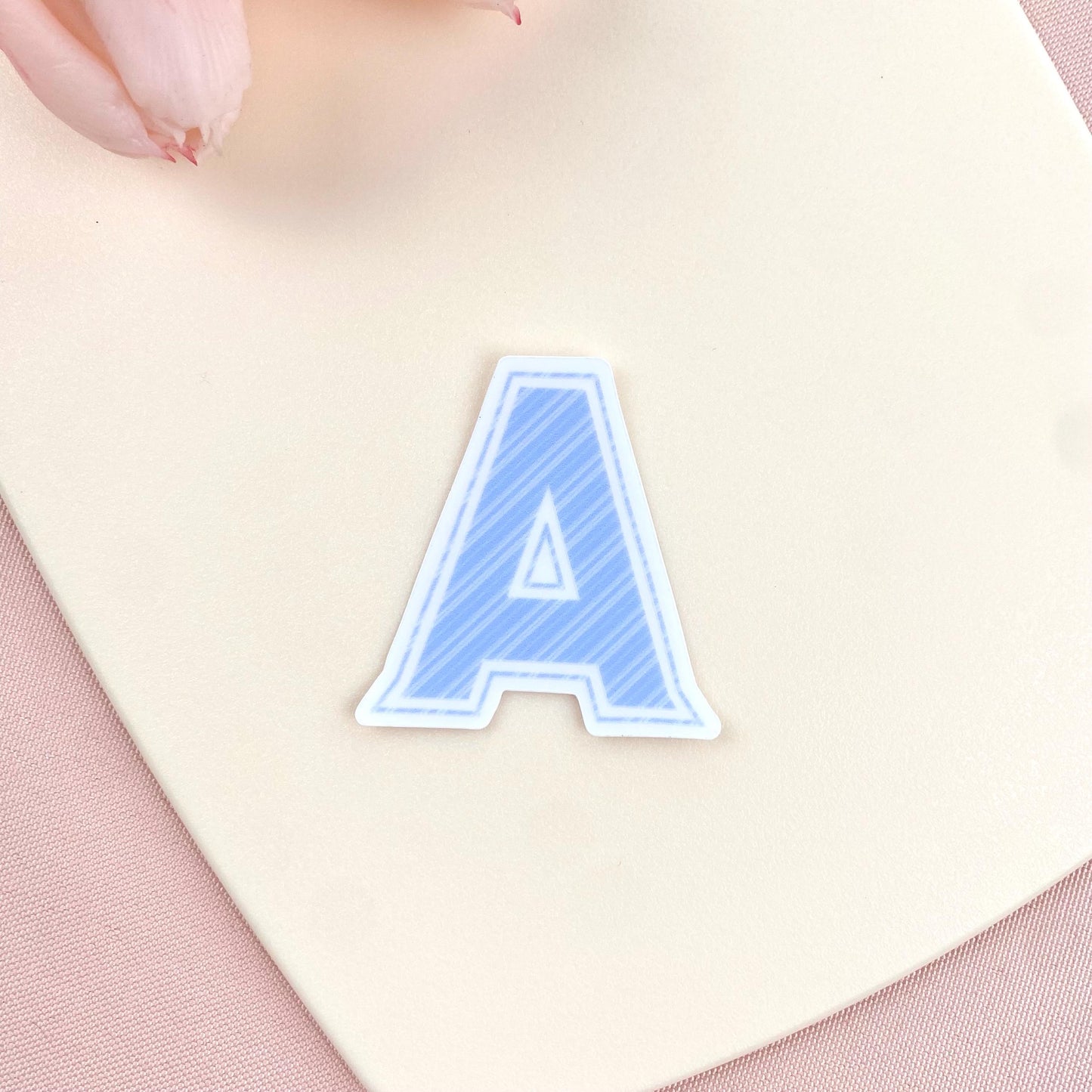 Blue striped letter 'A' sticker on a pink and beige background