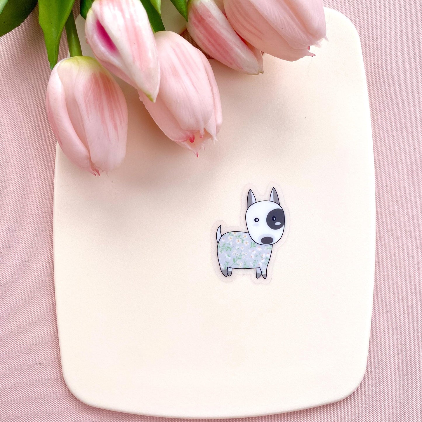 Sticker with a dog illustration on a pink surface with pink tulips.