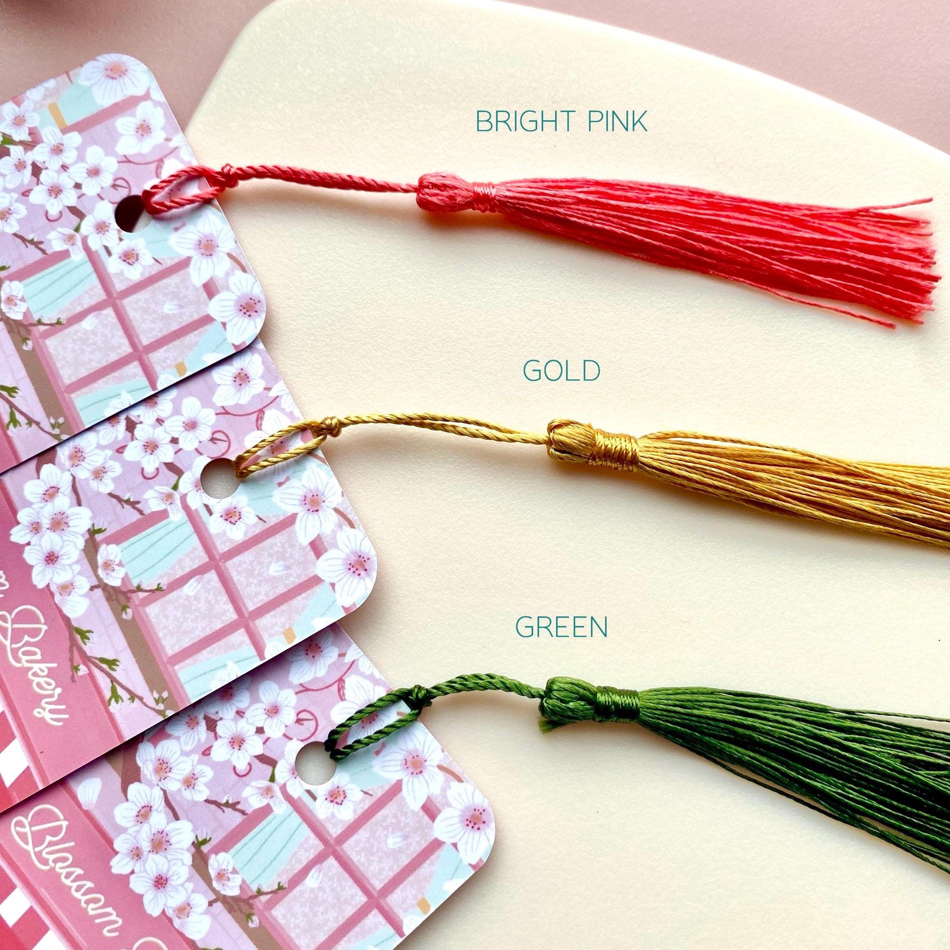 Matching bookmarks with tassels in bright pink, gold, and green on a light background.