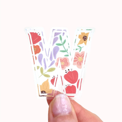 Hand holding a floral sticker of a letter 'W' on a white background
