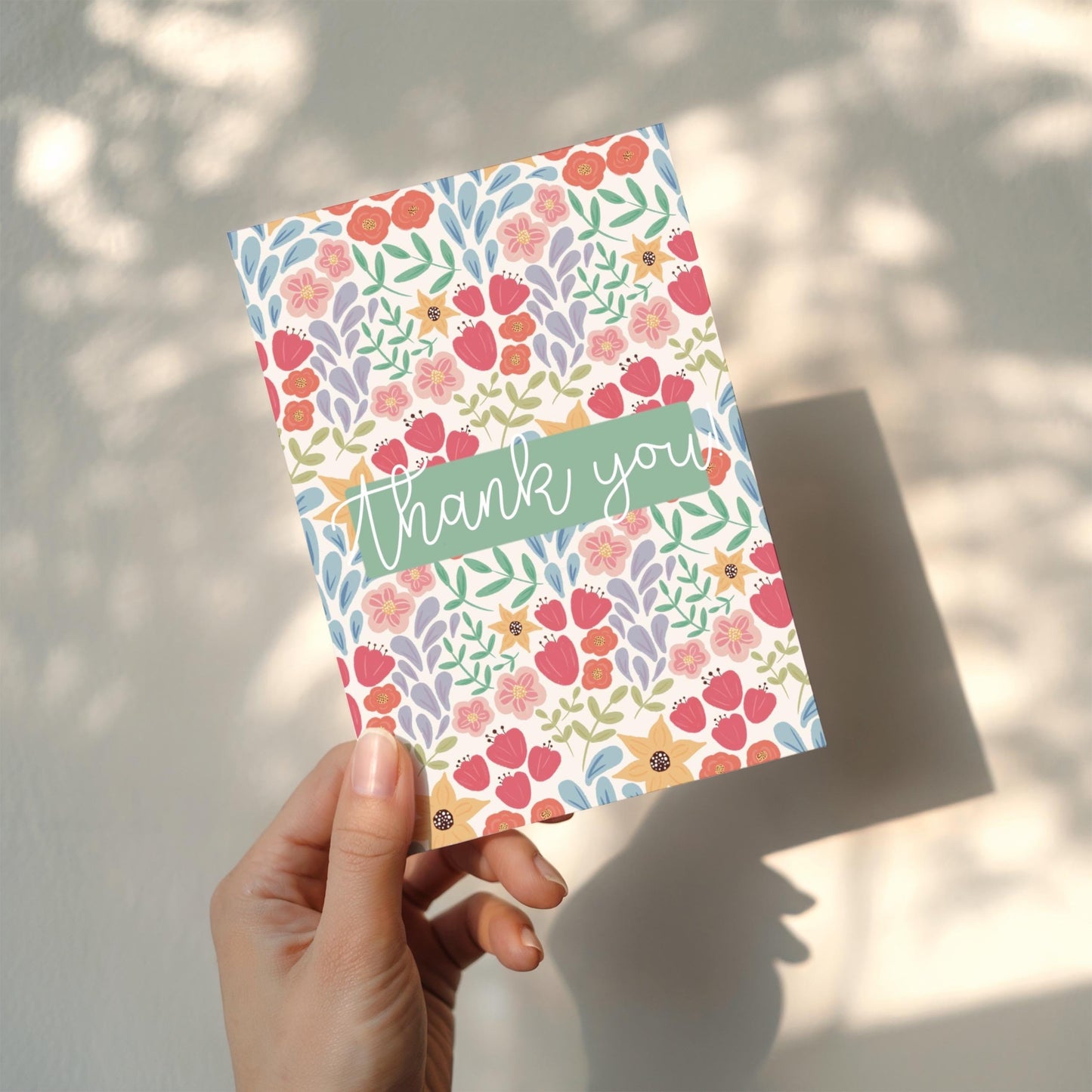 Floral card with 'thank you' text held by a hand against a light background