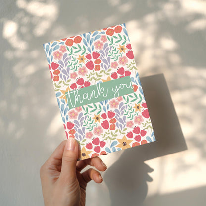 Floral card with 'thank you' text held by a hand against a light background