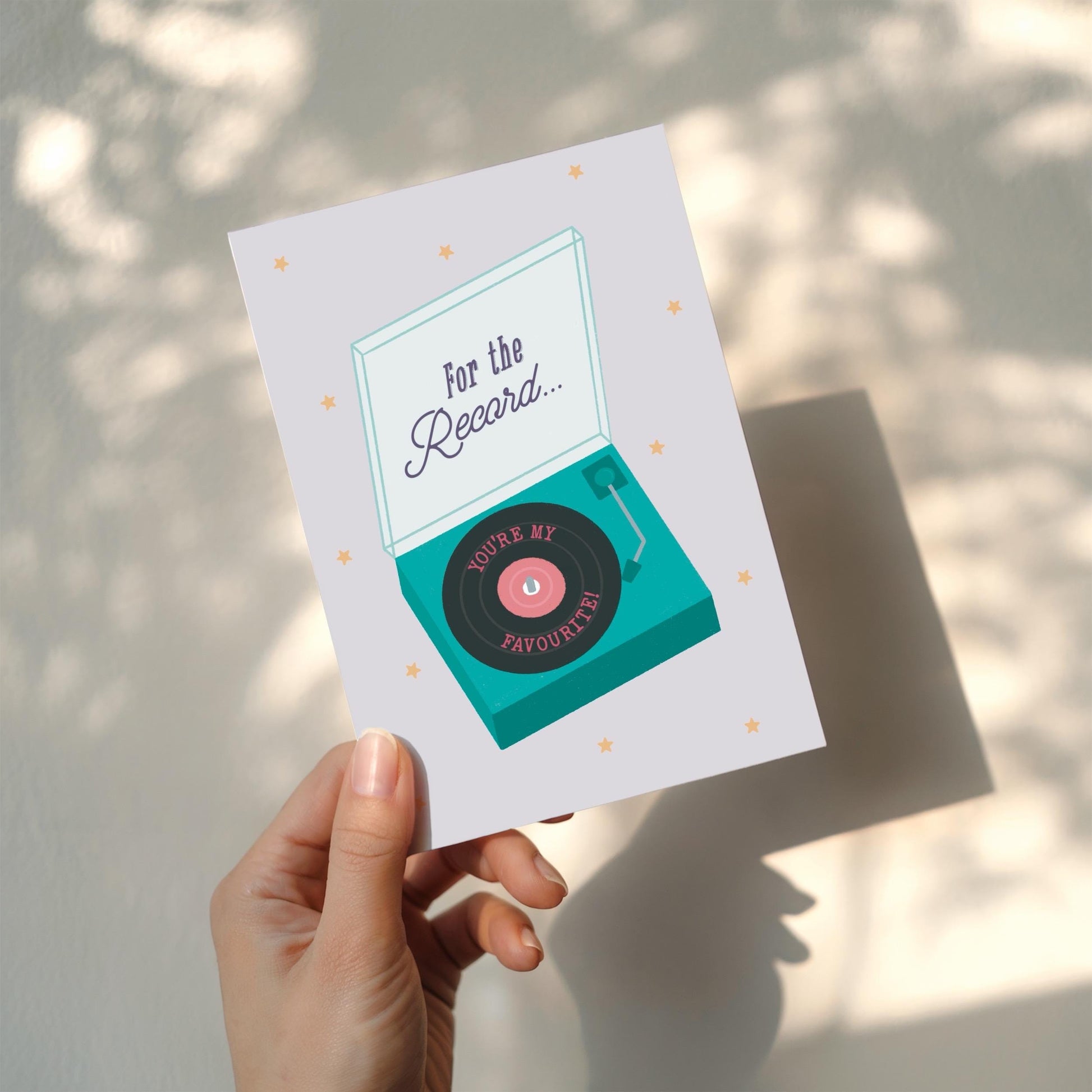 Greeting card with record player design  and 'For the record... you're my favourite' message being held up by hand against a white wall.