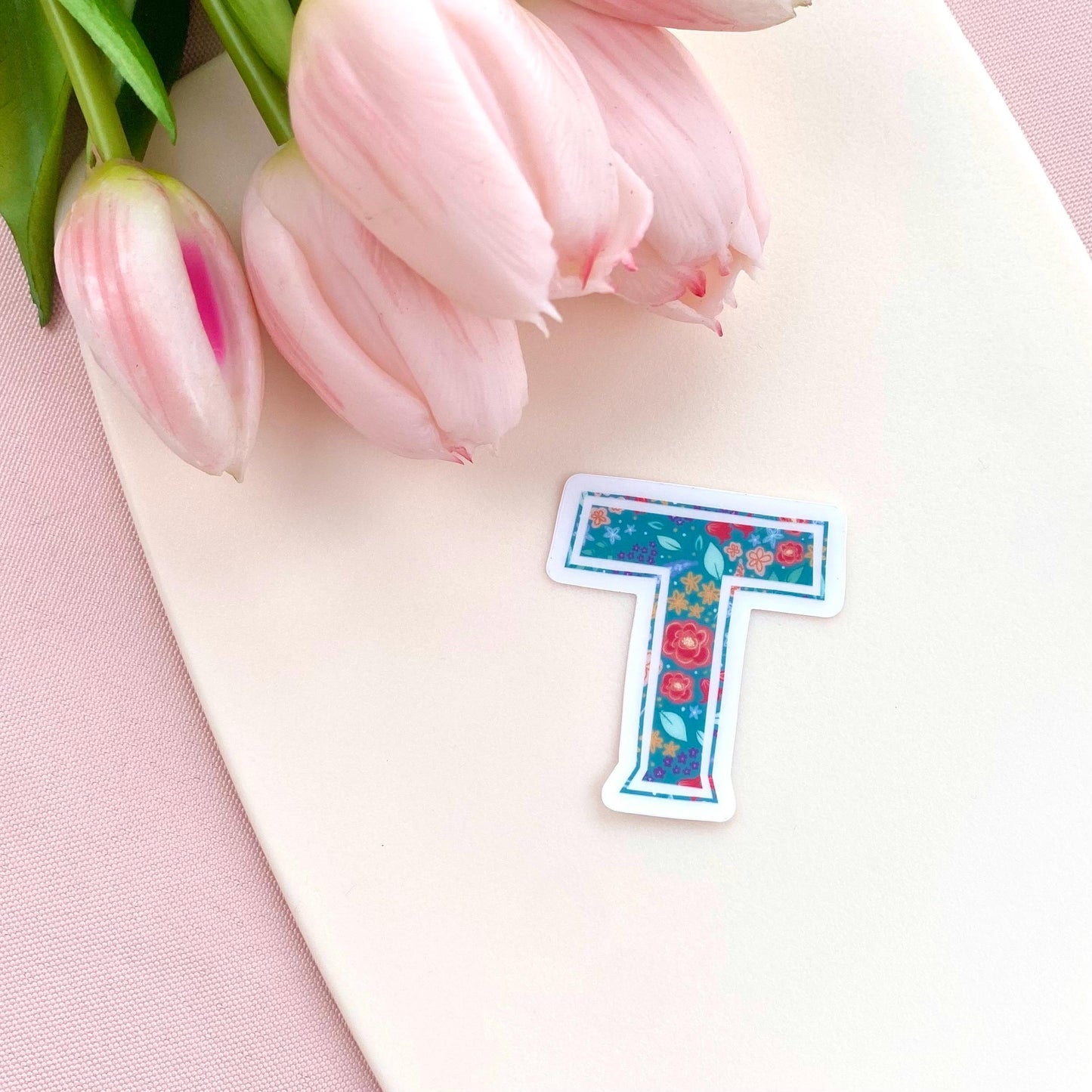 Floral letter 'T' sticker with pink tulips on a pink background