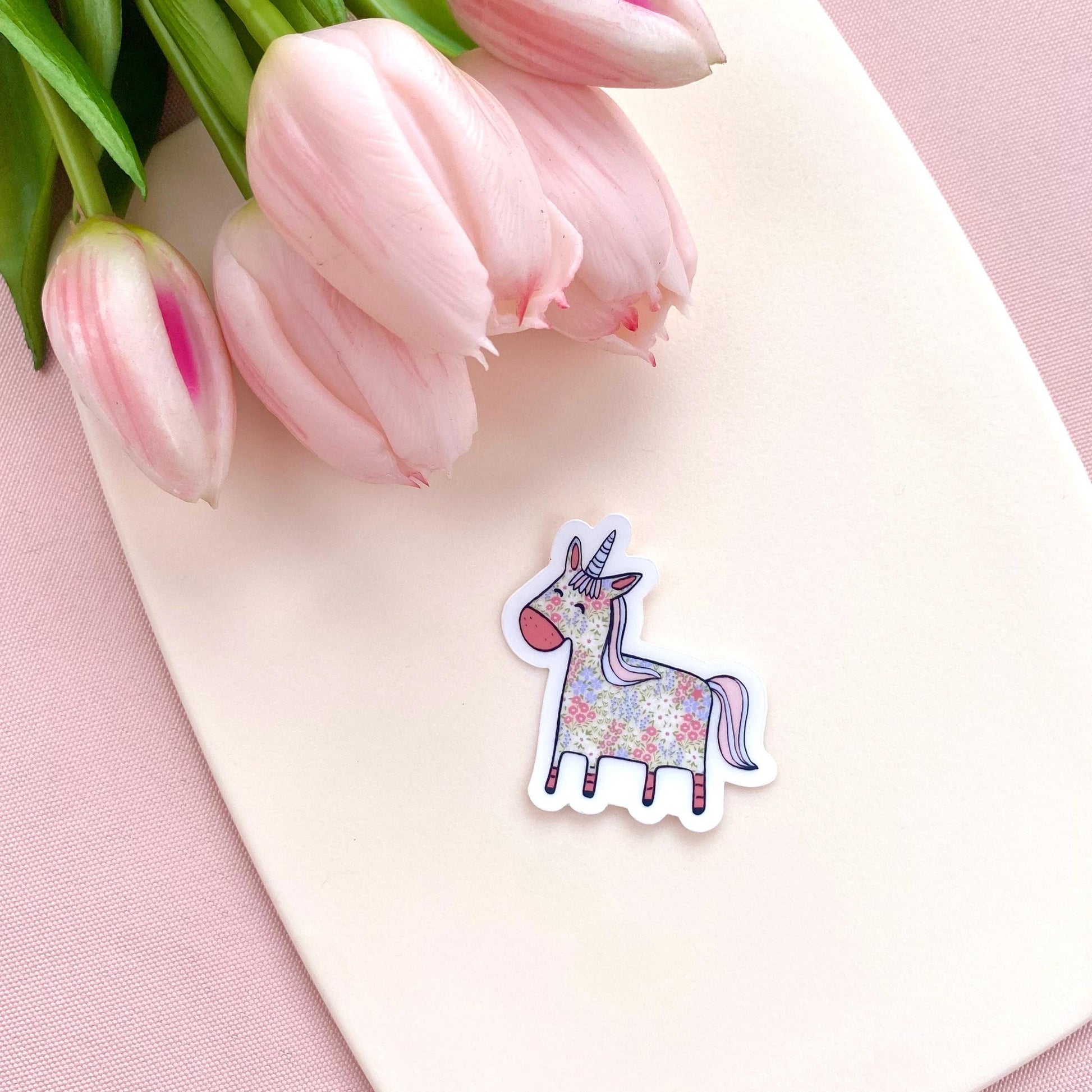 Floral patterned pink and blue unicorn on a transparent vinyl sticker against a white background with pink tulips