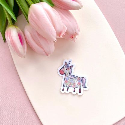 Floral patterned pink and blue unicorn on a transparent vinyl sticker against a white background with pink tulips