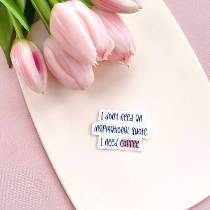 Clear vinyl sticker with black text 'I don't need an inspirational quote, I need coffee' shown on a white background with pink tulips
