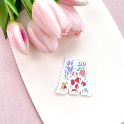 Decorative letter 'M' sticker with floral patterns on a white background with pink tulips