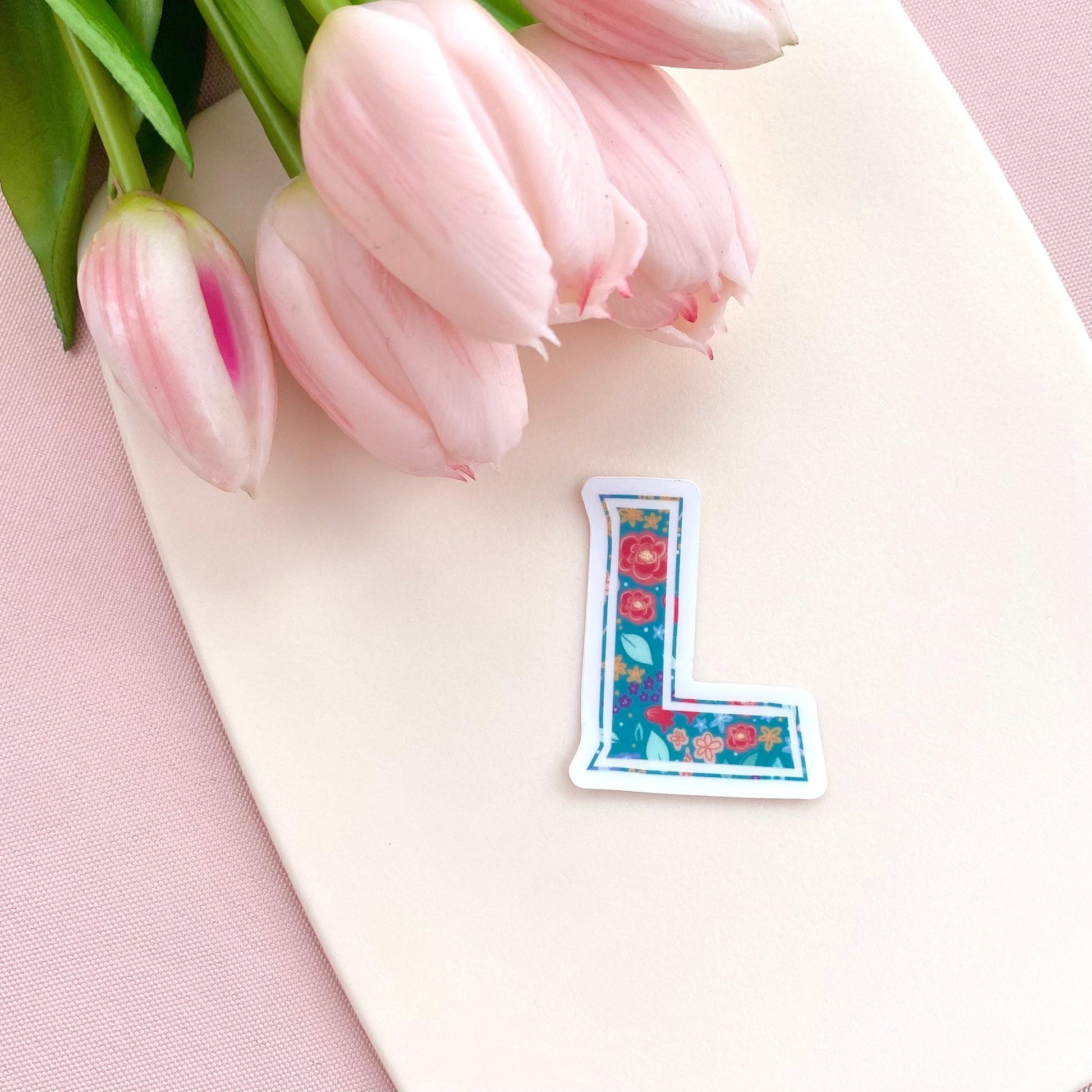 Floral letter 'L' sticker on a pink surface with pink tulips
