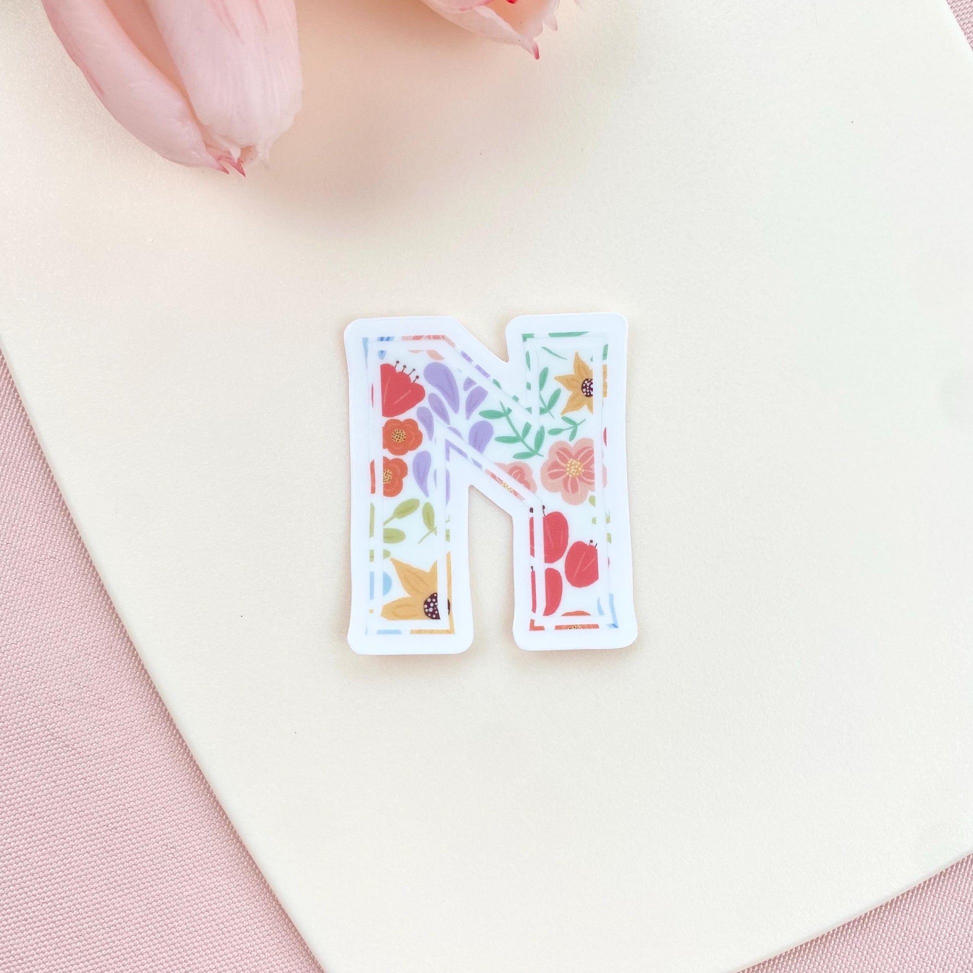 Floral letter 'N' sticker on a soft pink background