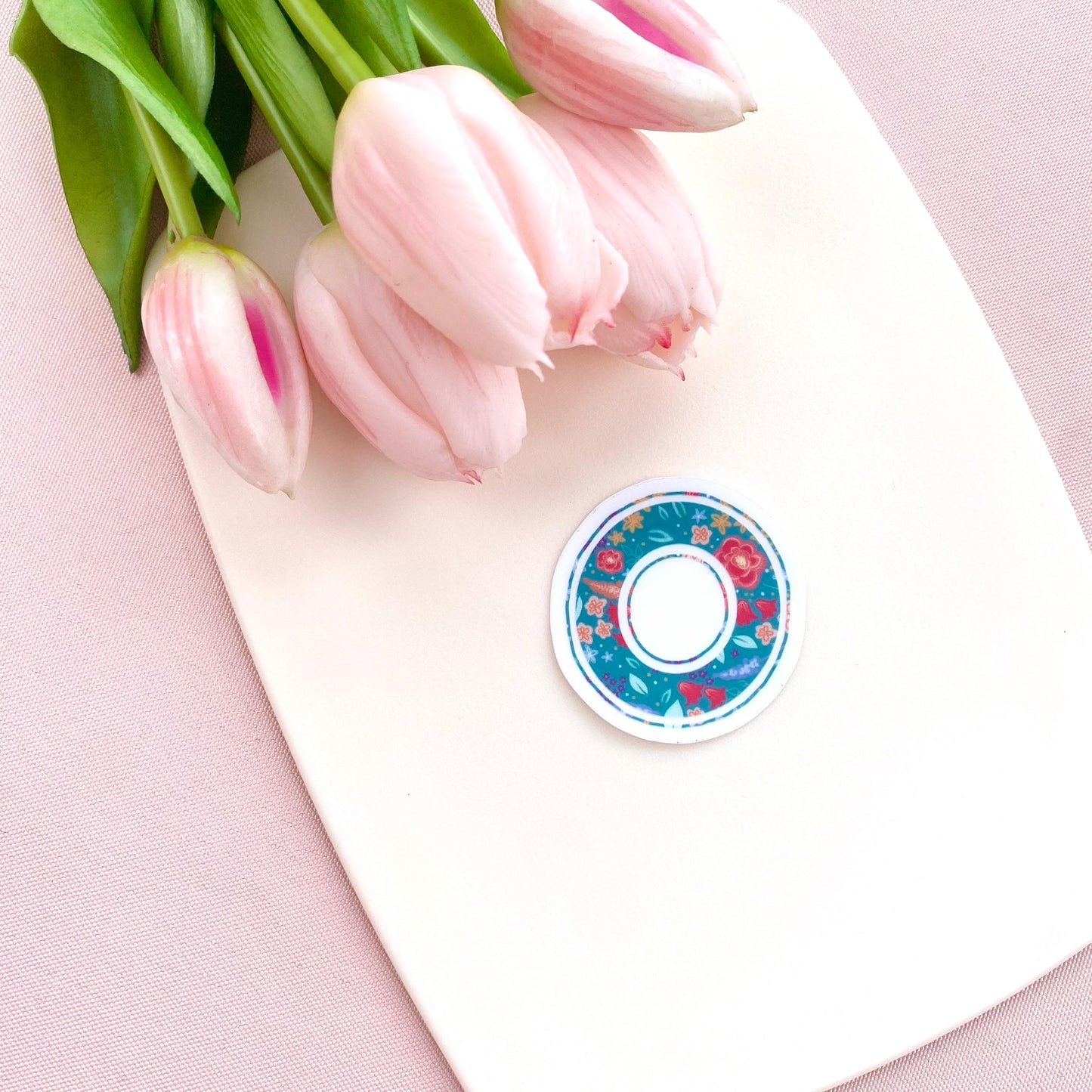 Decorative letter 'O' sticker with floral pattern held on a white background with pink tulips