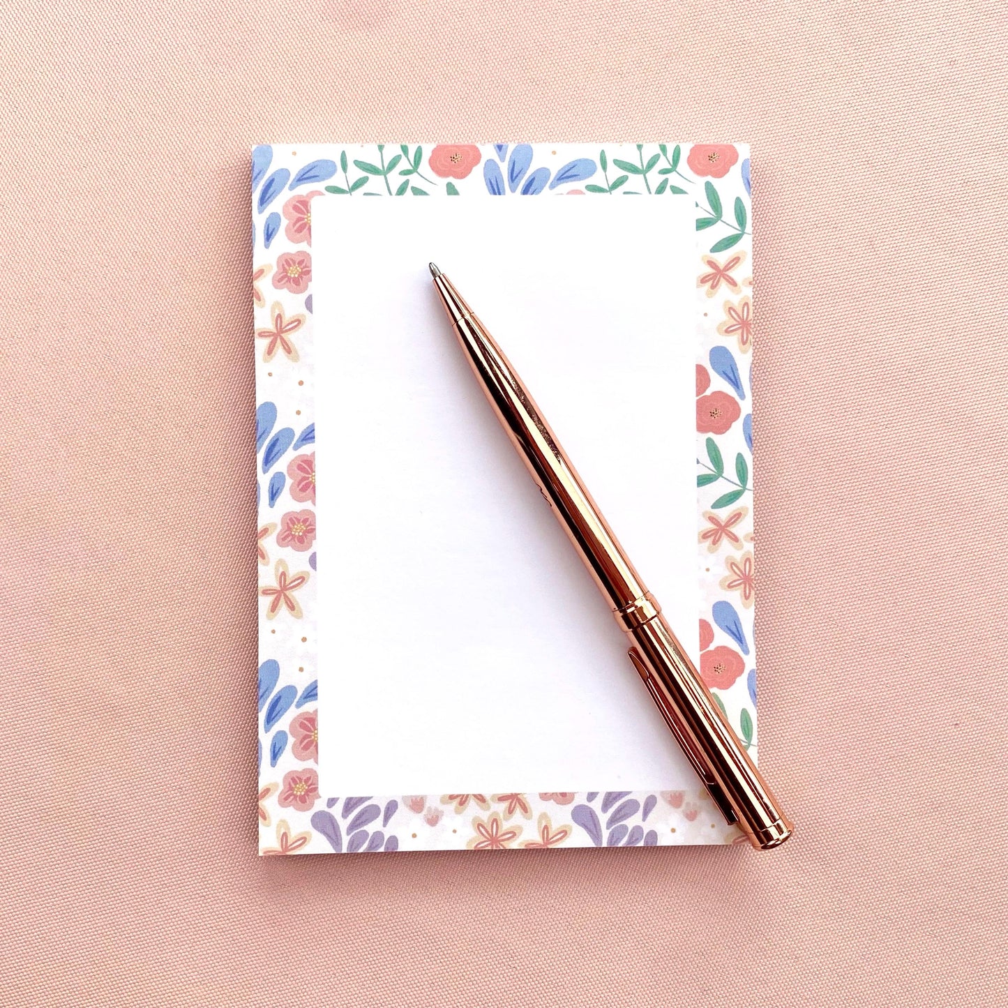Floral notebook with a rose gold pen on a pink background