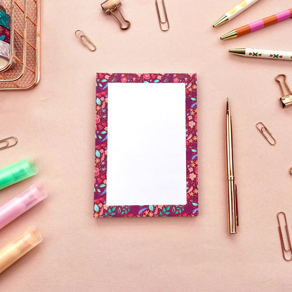 Floral-patterned notepad with stationery items on a pink background