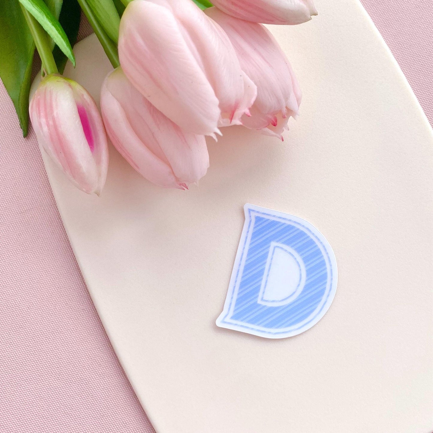Pink tulips on a white surface with a blue striped letter 'D' vinyl sticker.