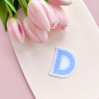 Pink tulips on a white surface with a blue striped letter 'D' vinyl sticker.