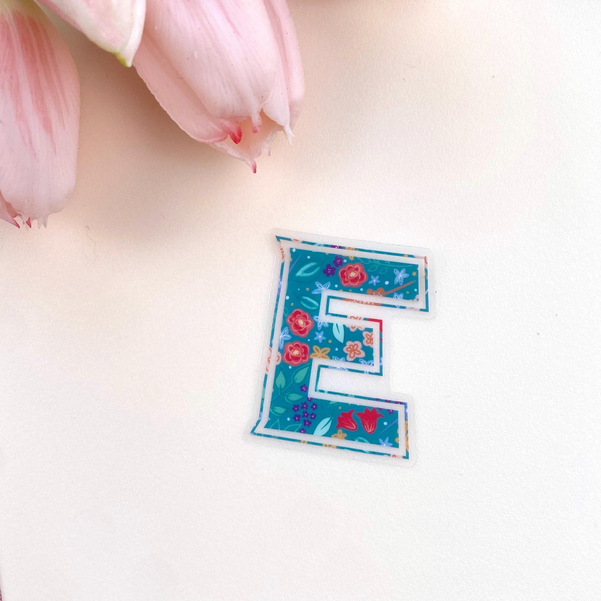 Floral letter 'E' sticker on a cream surface with pink tulips