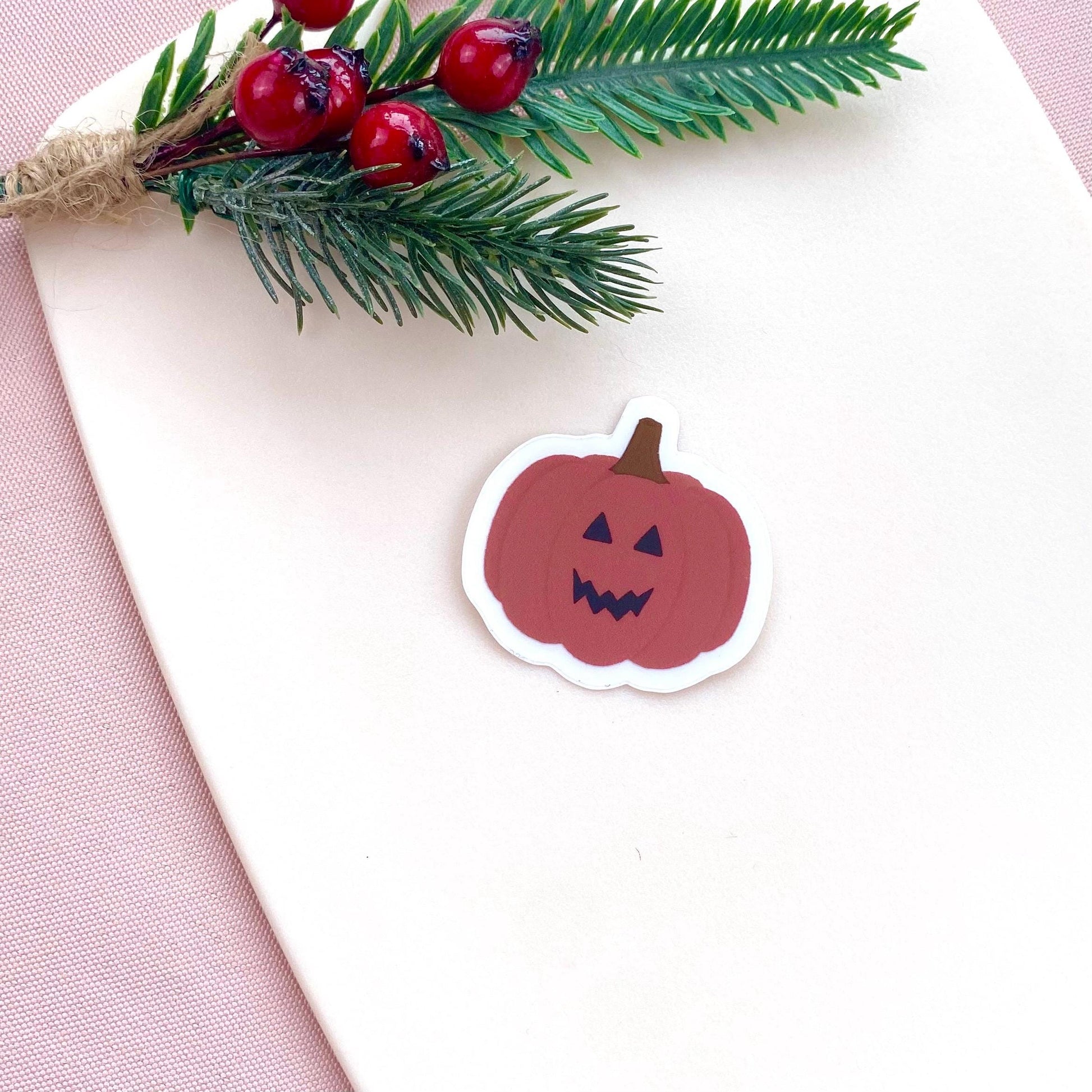 Sticker of a pink jack-o'-lantern with greenery on a white background