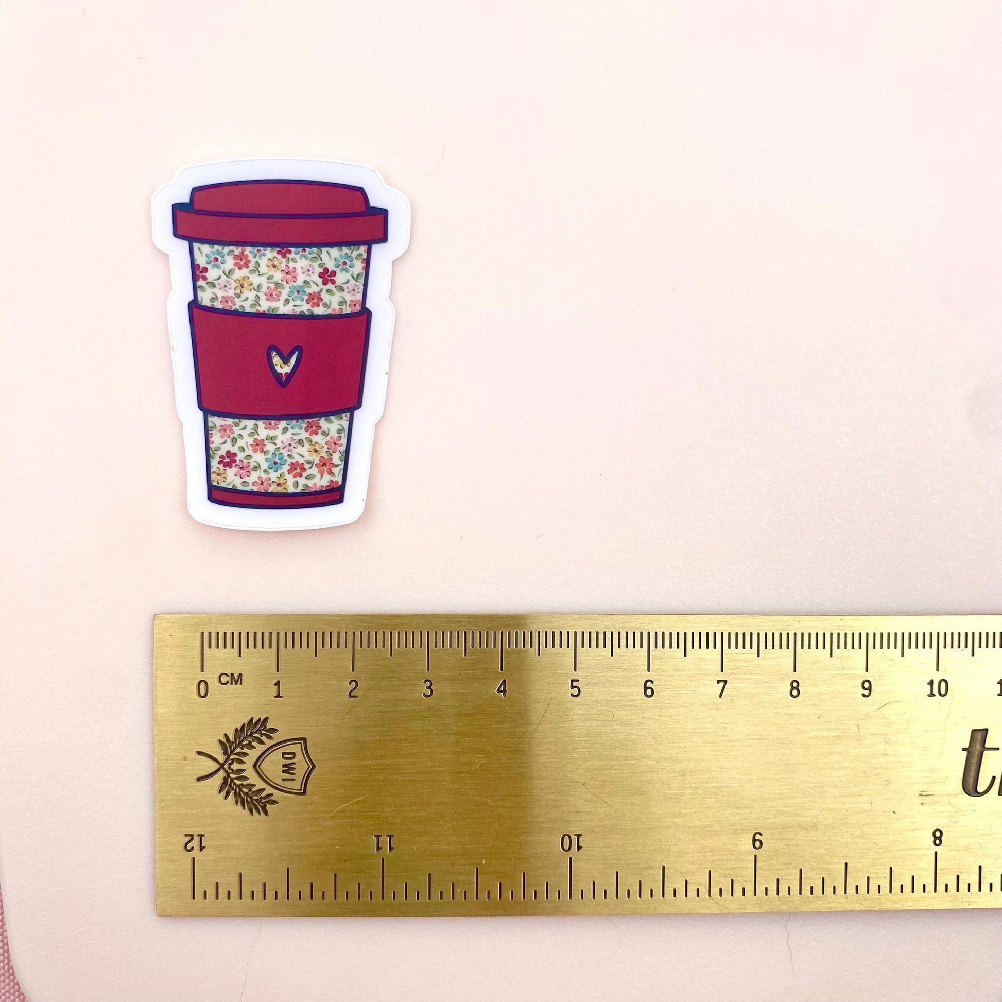 Floral-patterned coffee cup sticker next to a ruler on a beige background